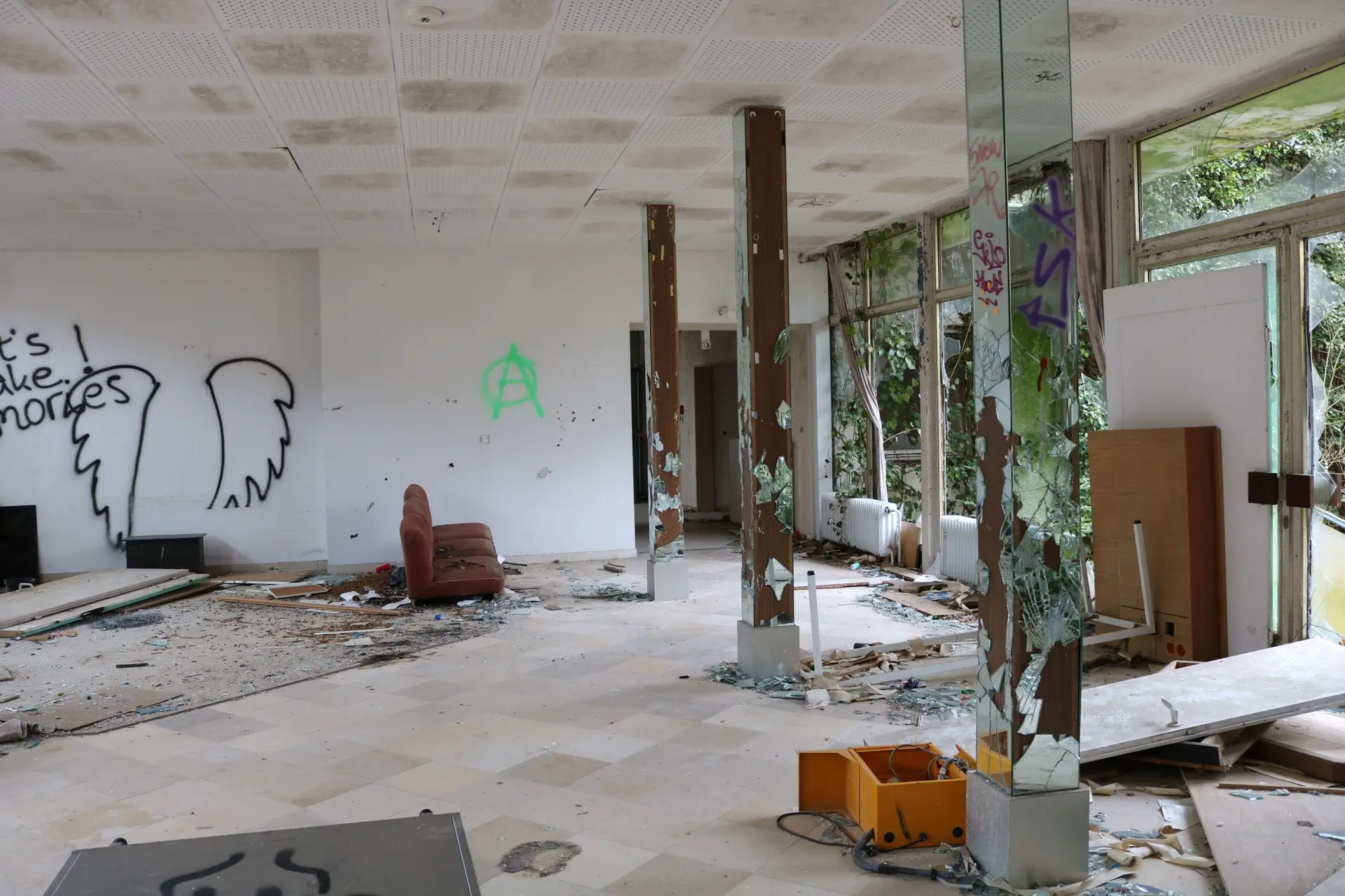 Startseite An abandoned room with broken windows, graffiti on white walls, and scattered debris.